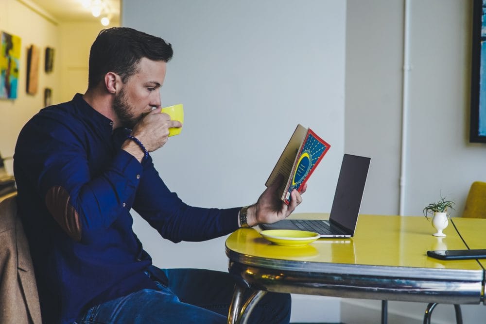 Man drinking coffee while reading a book