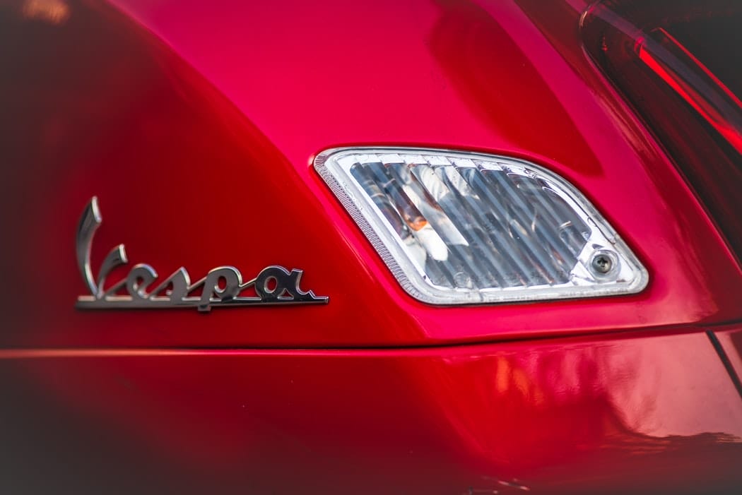 "Vespa" written in silver on the side of red scooter